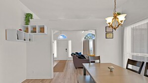 Un soggiorno moderno con zona pranzo, pavimento in legno, un lampadario e vista attraverso una finestra con tende.