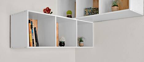 Pared blanca con un estante empotrado que contiene libros, pequeñas macetas y un objeto decorativo.