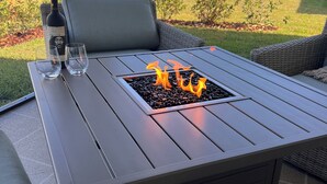 Un patio con una mesa, dos sillas, una botella de vino y copas.