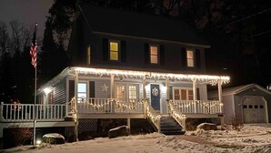 A two-story house with a porch decorated with string lights and a wreath on the door. - Charming Country Home w/Character of the Adirondacks (Lake Placid)