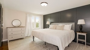 A bedroom with a large bed, bedside tables with lamps, a dresser, and a window with curtains. - Kid-Friendly 4 Bedroom Home w/ Heated Private Pool (Overland Park)