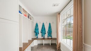 A clean, modern locker room with a bench and lockers, a large window with curtains, and a tiled floor. - Kid-Friendly 4 Bedroom Home w/ Heated Private Pool (Overland Park)