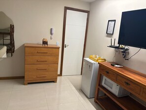 Eine kleine Küchenzeile mit einem Holzkorpus, einem Kühlschrank, einer Mikrowelle und einem an der Wand befestigten Fernseher.