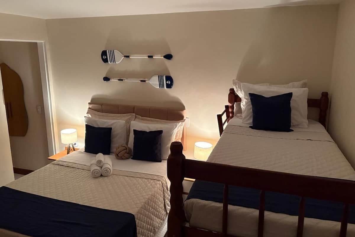 A hotel room with two beds, each with a wooden headboard, a bedside table with a lamp, and a wall-mounted rack with towels.