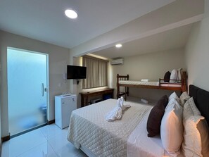 Una habitación de hotel con cama, escritorio, televisión y aire acondicionado.