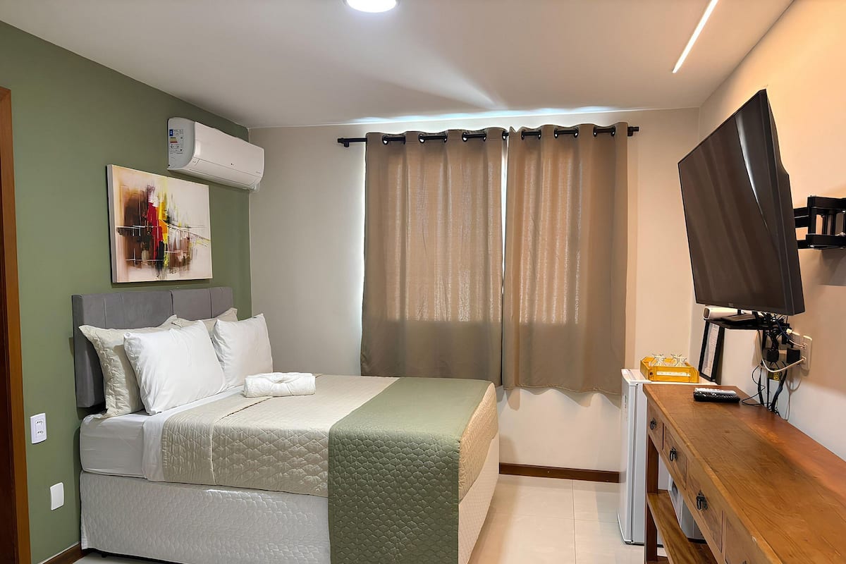 A bedroom with a bed, a TV, a dresser, and a window with curtains.