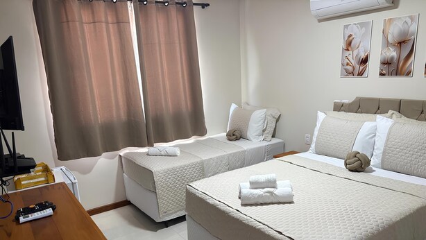 A hotel room with two single beds, a wooden desk with a computer, and a TV. - Suítes Brisa do Mar (Búzios)