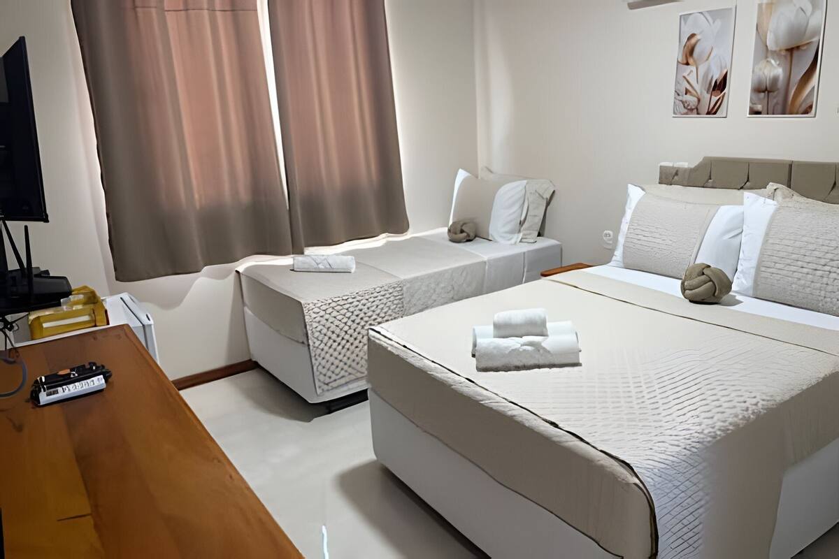 A hotel room with two single beds, a larger bed, a desk with a computer, and a TV.