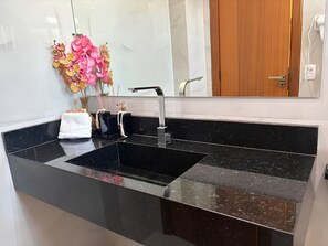 Un baño moderno con un lavamanos de mármol negro, un espejo y una puerta de madera.
