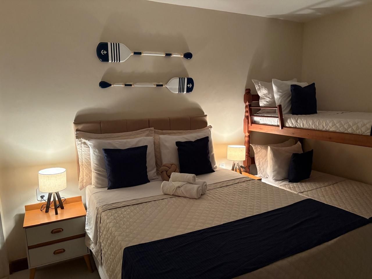 Habitación de hotel con dos camas, una mesita de noche con lámpara y un perchero en la pared con objetos.