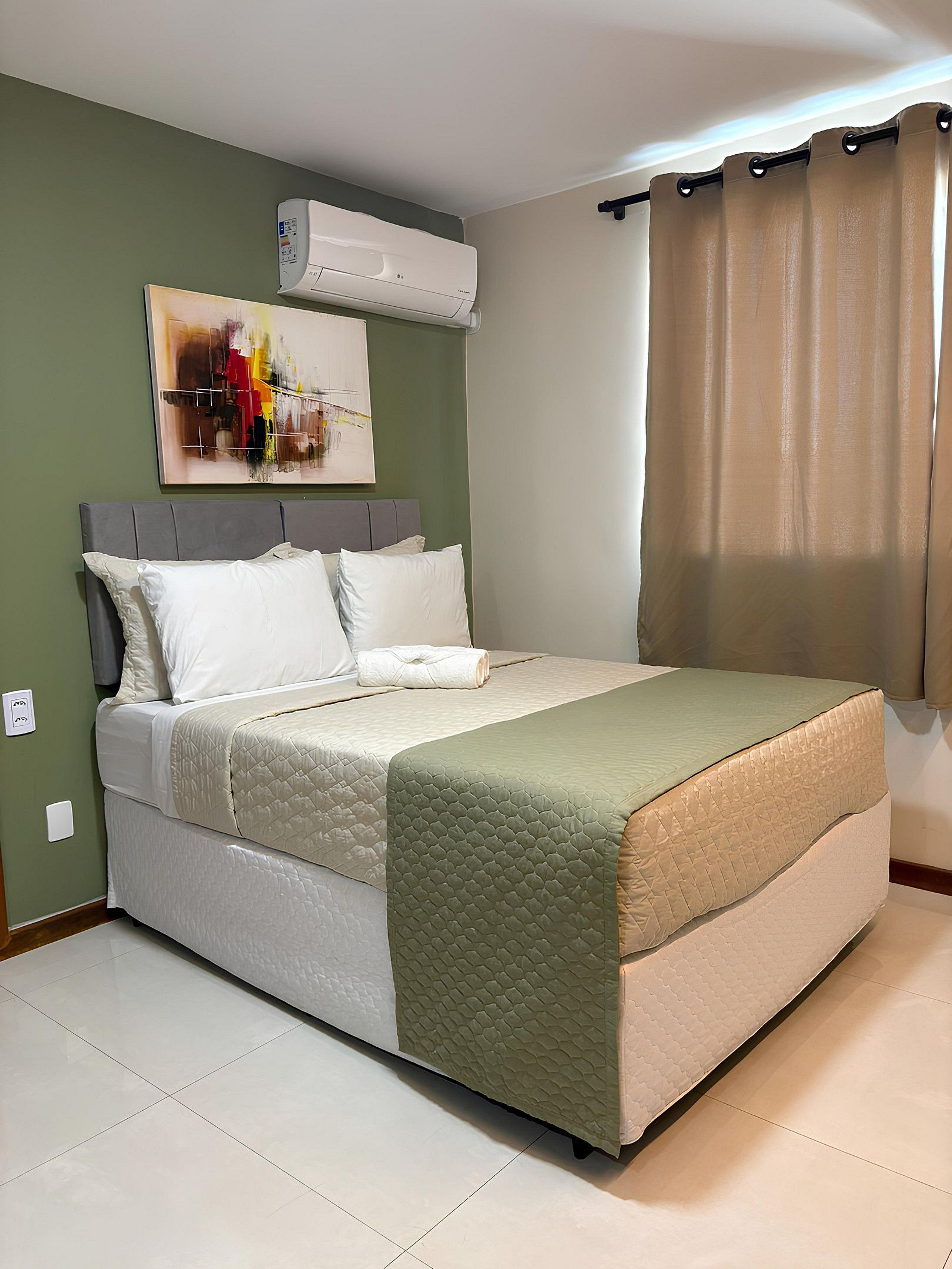 A bedroom with a bed, a headboard, a wall-mounted air conditioner, a painting, and a window with curtains.