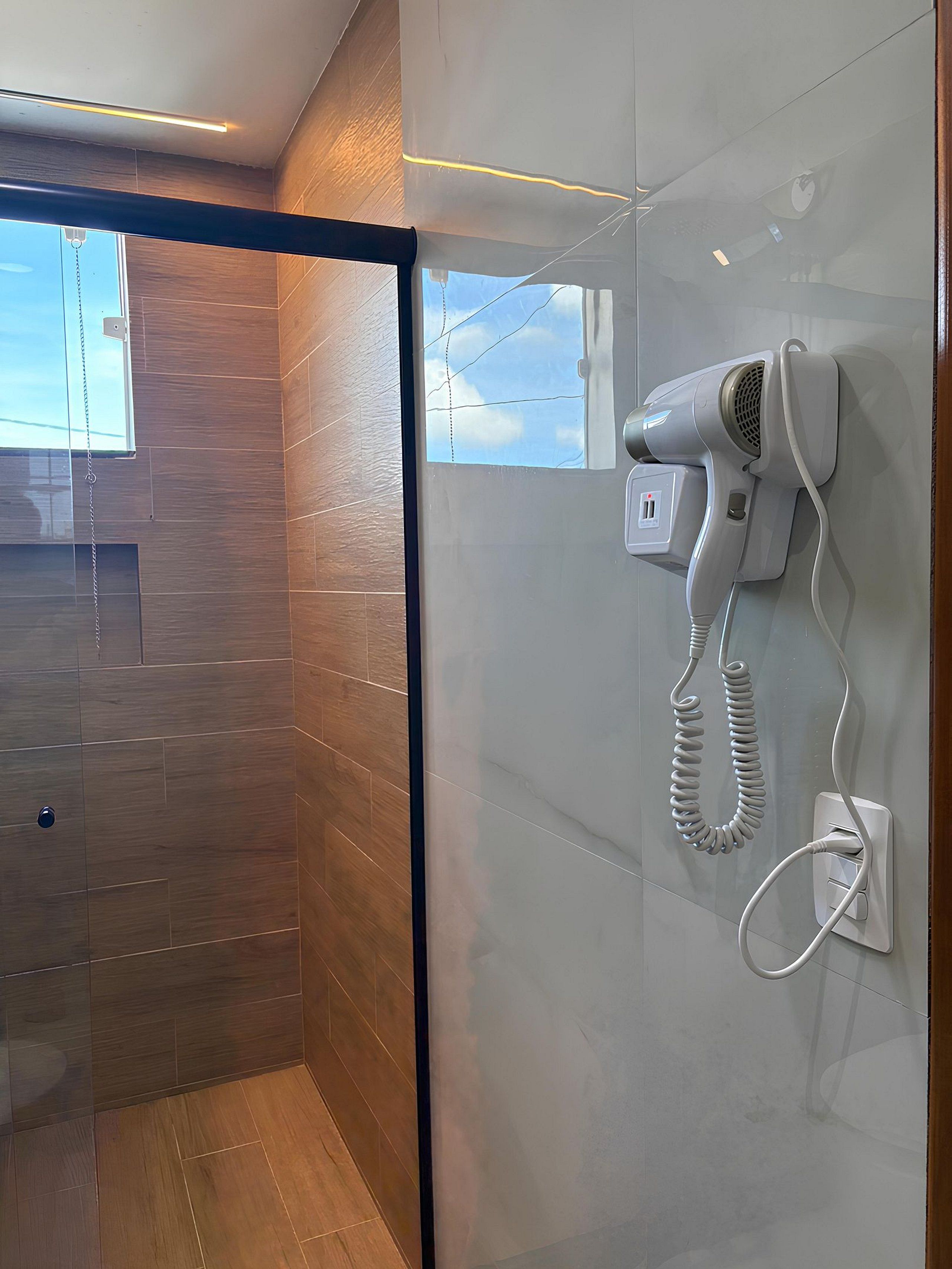 A modern bathroom with a hairdryer mounted on the wall, a wooden floor, and a glass shower enclosure.