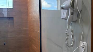 A modern bathroom with a hairdryer mounted on the wall, a wooden floor, and a glass shower enclosure.