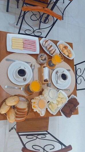 A breakfast table with plates of food, cups of coffee, and a basket of bread. - Suítes Brisa do Mar (Búzios)