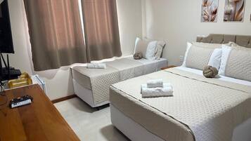 Ein Hotelzimmer mit zwei Einzelbetten, einem größeren Bett, einem Holztisch mit einer Fernbedienung und einem Fernseher.