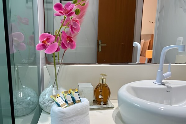 A bathroom with a white sink, a mirror, and a vase with pink flowers. - Suítes Brisa do Mar (Búzios)