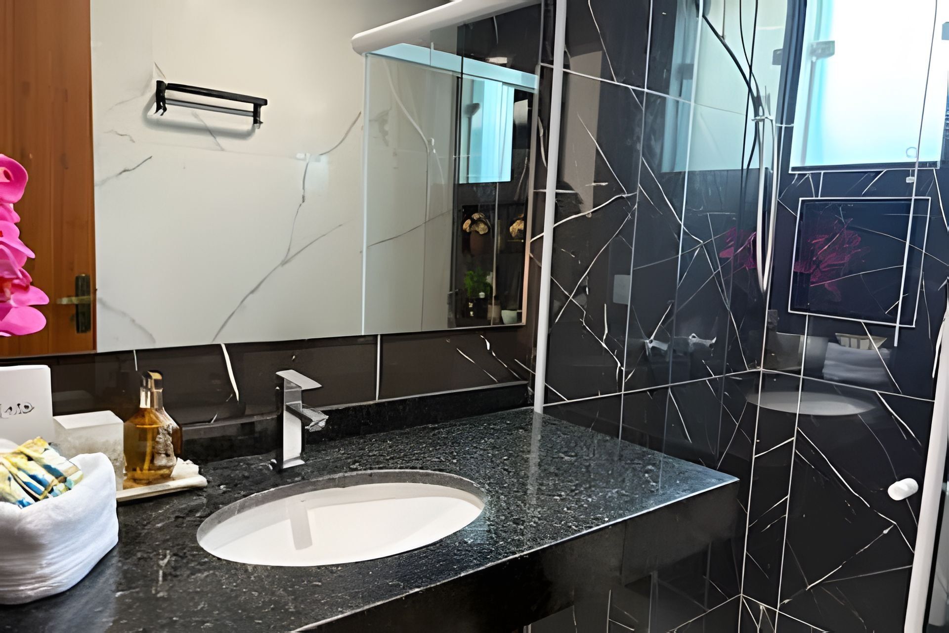 A modern bathroom with a black marble sink, a large mirror, and a glass shower enclosure.