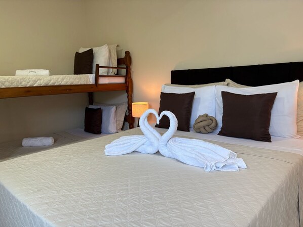 A hotel room with a bunk bed, a neatly made bed with a towel art, and a lamp on the nightstand. - Suítes Brisa do Mar (Búzios)
