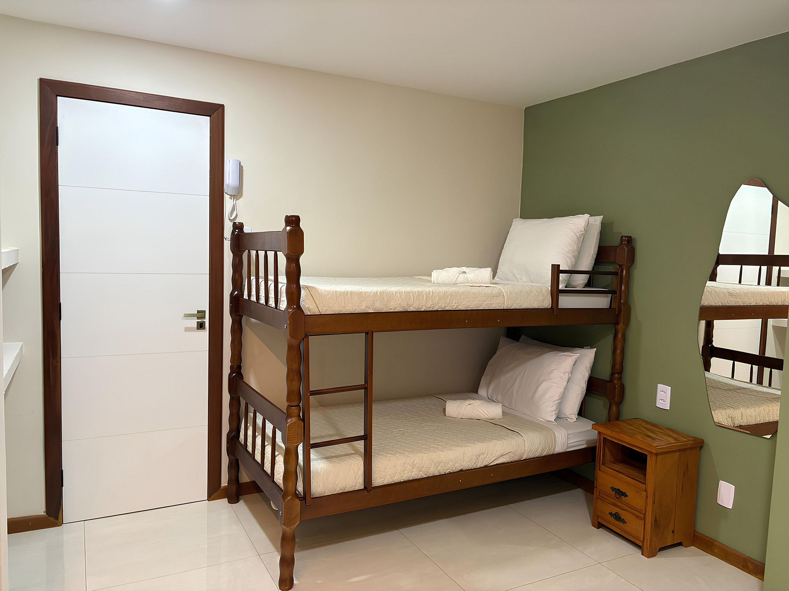 A bunk bed room with a wooden frame, a small wooden nightstand, and a white door.