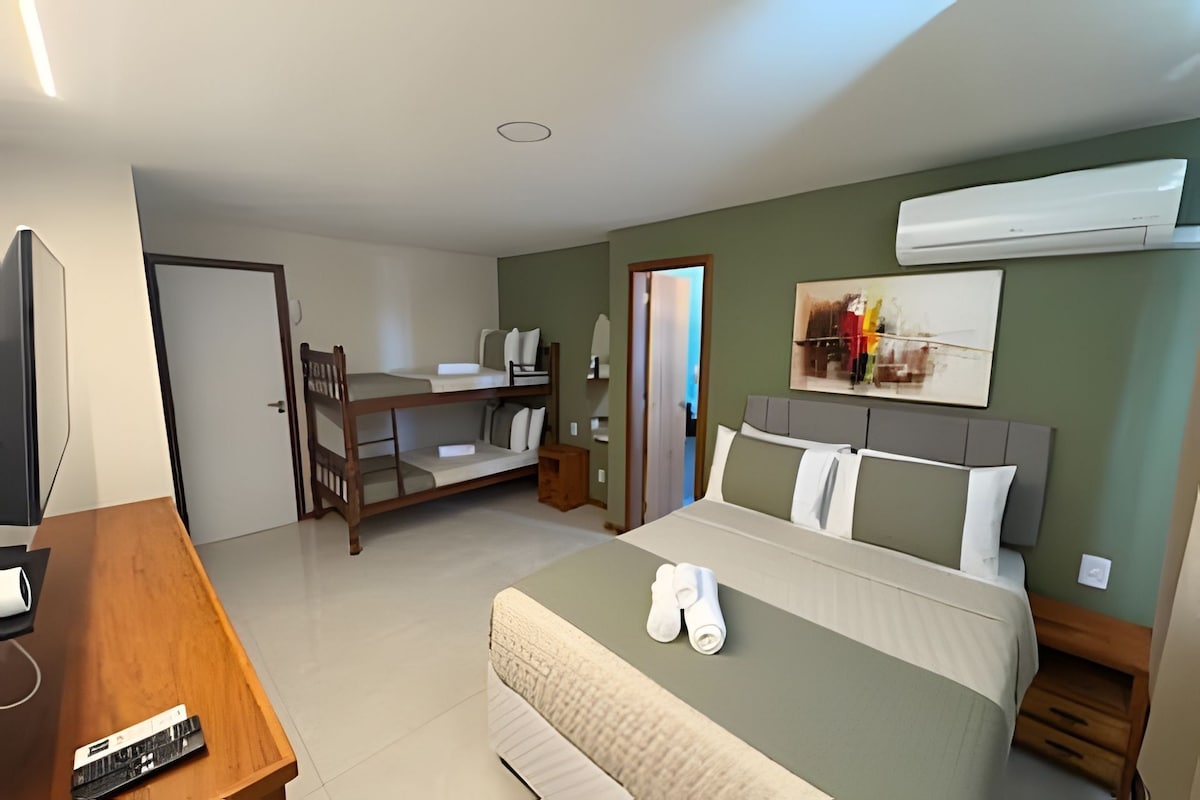 Habitación de hotel con cama, escritorio, silla, televisor y aire acondicionado.