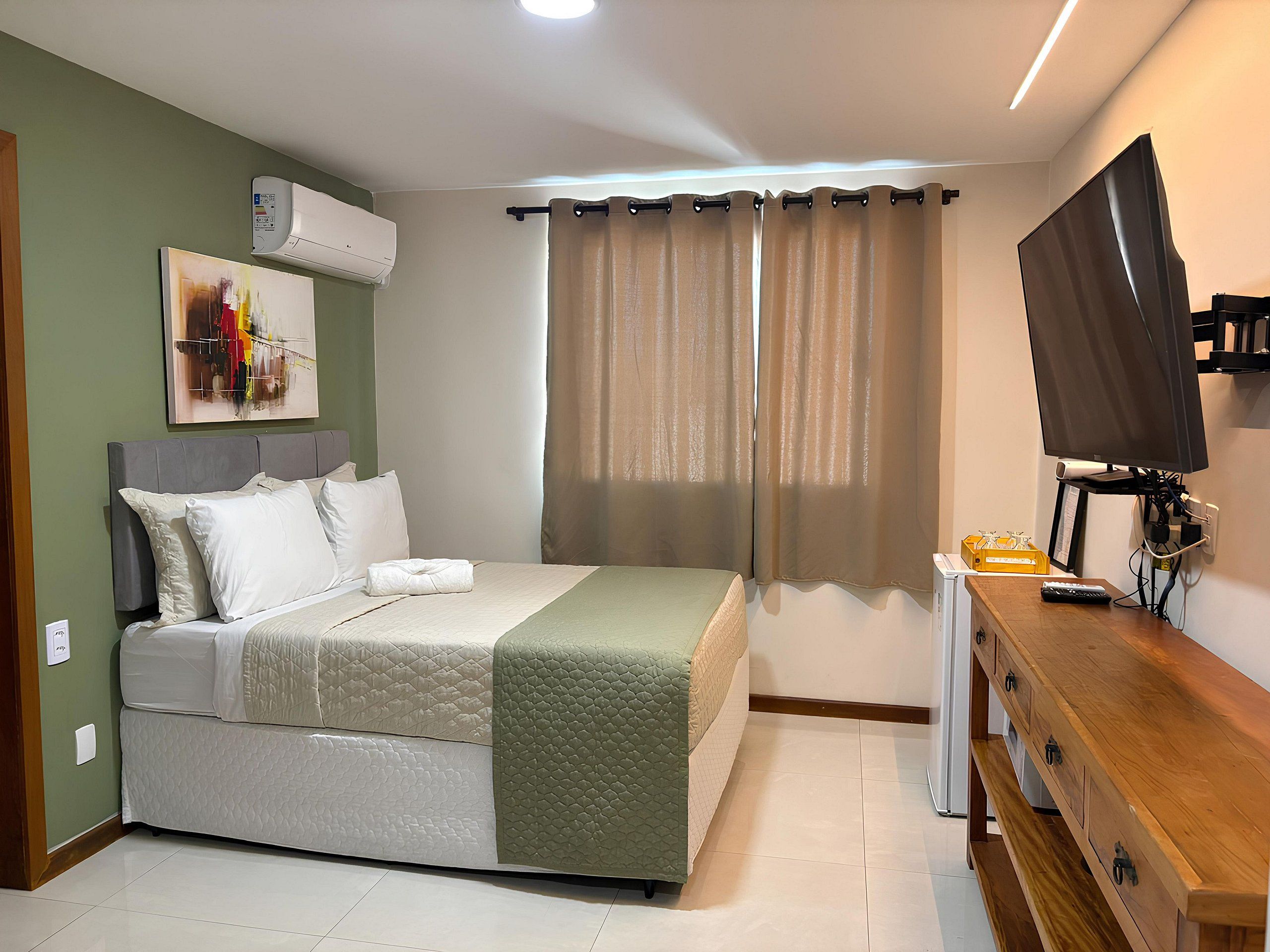 A bedroom with a bed, a TV, a dresser, and a window with curtains.