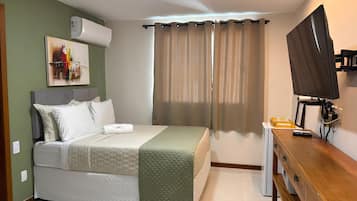A bedroom with a bed, a TV, a dresser, and a window with curtains.
