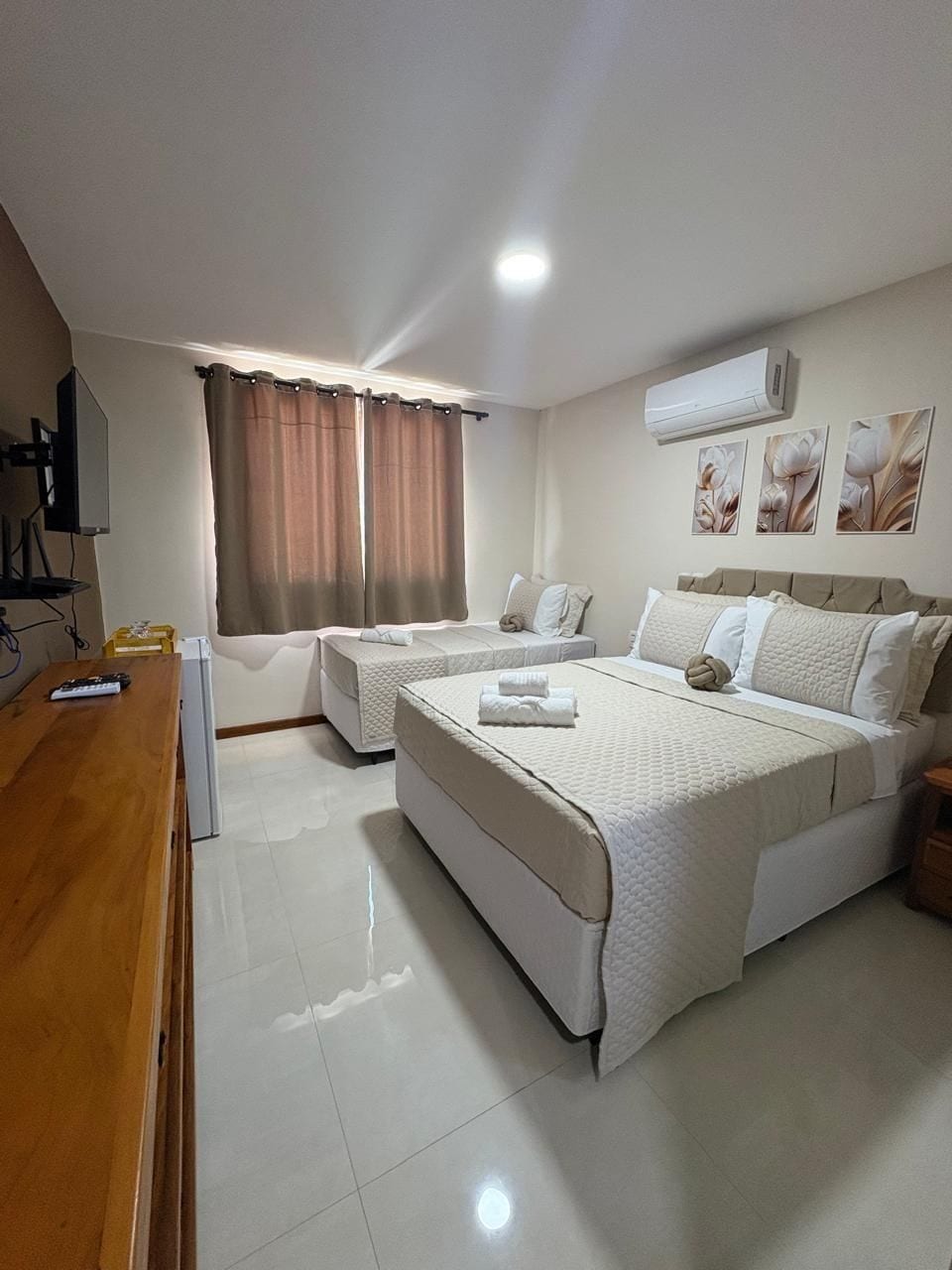 Quarto de hotel com duas camas, uma secretária de madeira, uma TV e um ar condicionado.