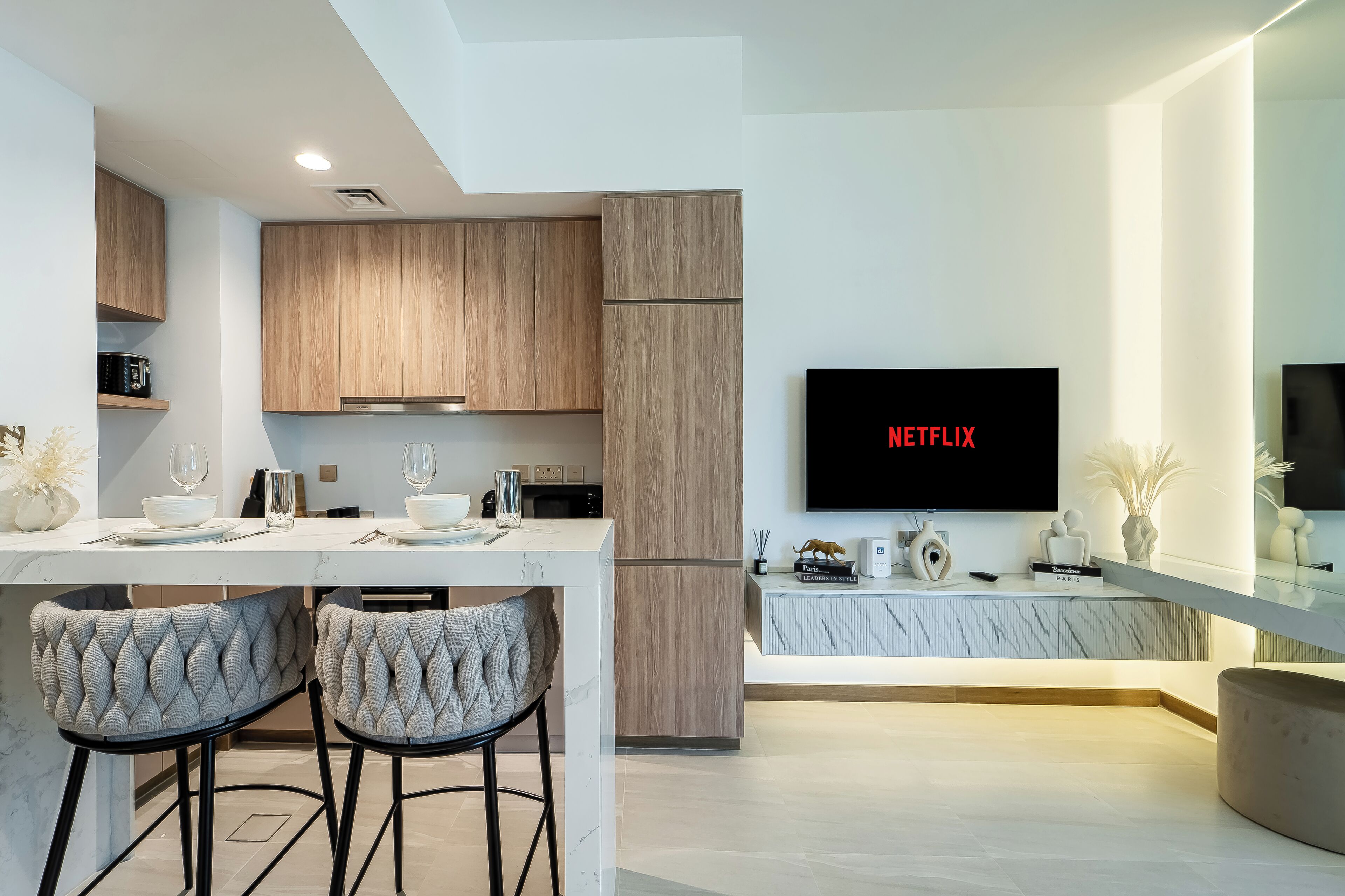Ett modernt kök med träskåp, en bänkskiva i marmor och en inbyggd tv som visar ”NETFLIX”.