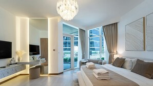 A modern hotel room with a large bed, a flat-screen TV, a desk, and a balcony with a view of the city.