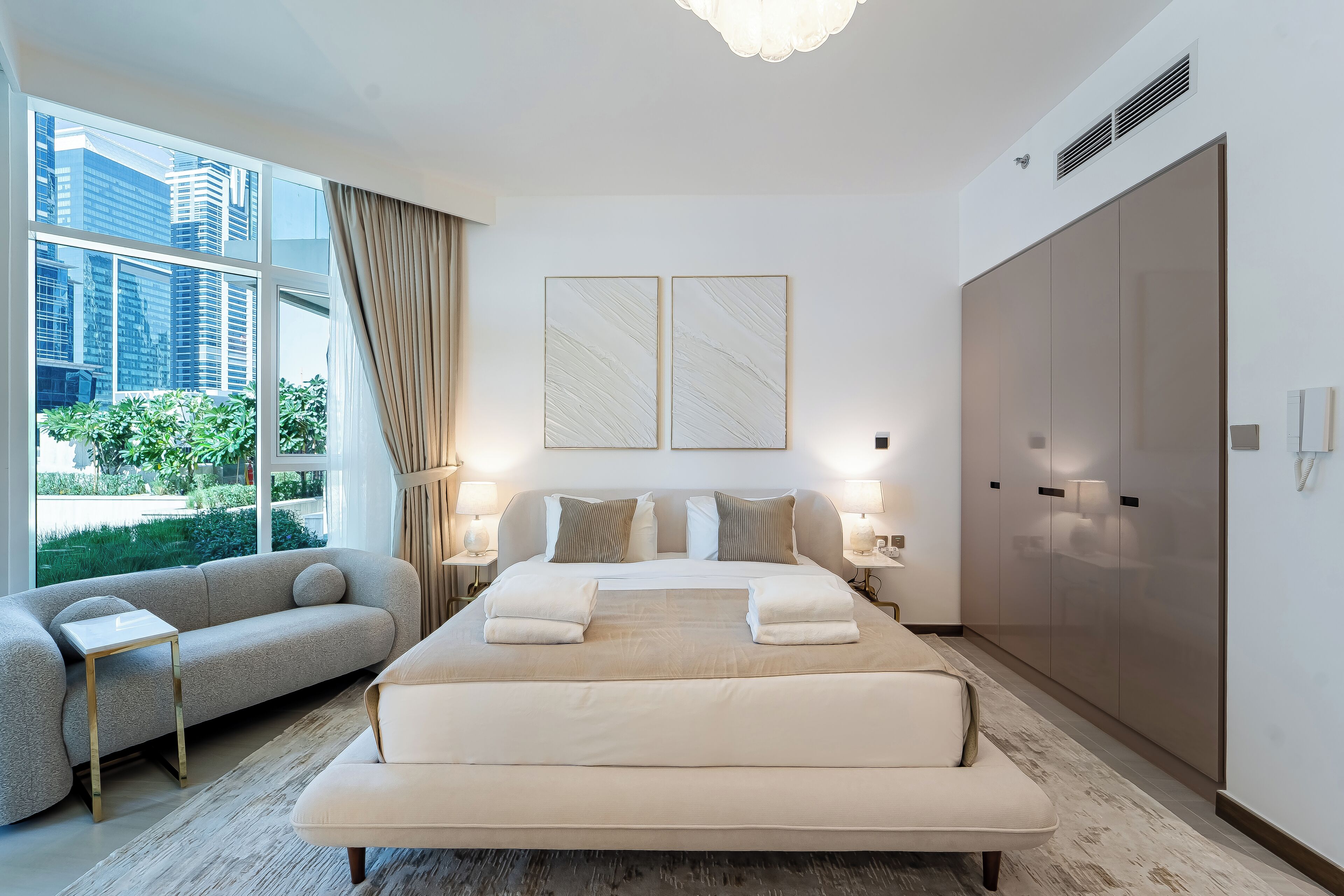 Una habitación de hotel moderna con una cama grande, un sofá y vistas de la ciudad a través de amplios ventanales.