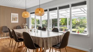 A dining area with a round table, six chairs, and a large window with a view of greenery. - 3 bedroom beautiful home in Gilleleje (Gilleleje)