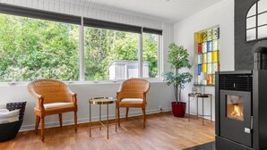 A room with two wicker chairs, a small table, a potted plant, a fireplace, and large windows with a view of greenery. - 3 bedroom beautiful home in Gilleleje (Gilleleje)