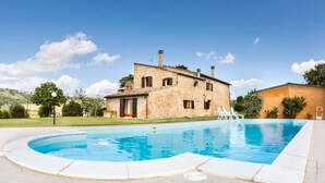 A stone house with a swimming pool, surrounded by a grassy area and trees.