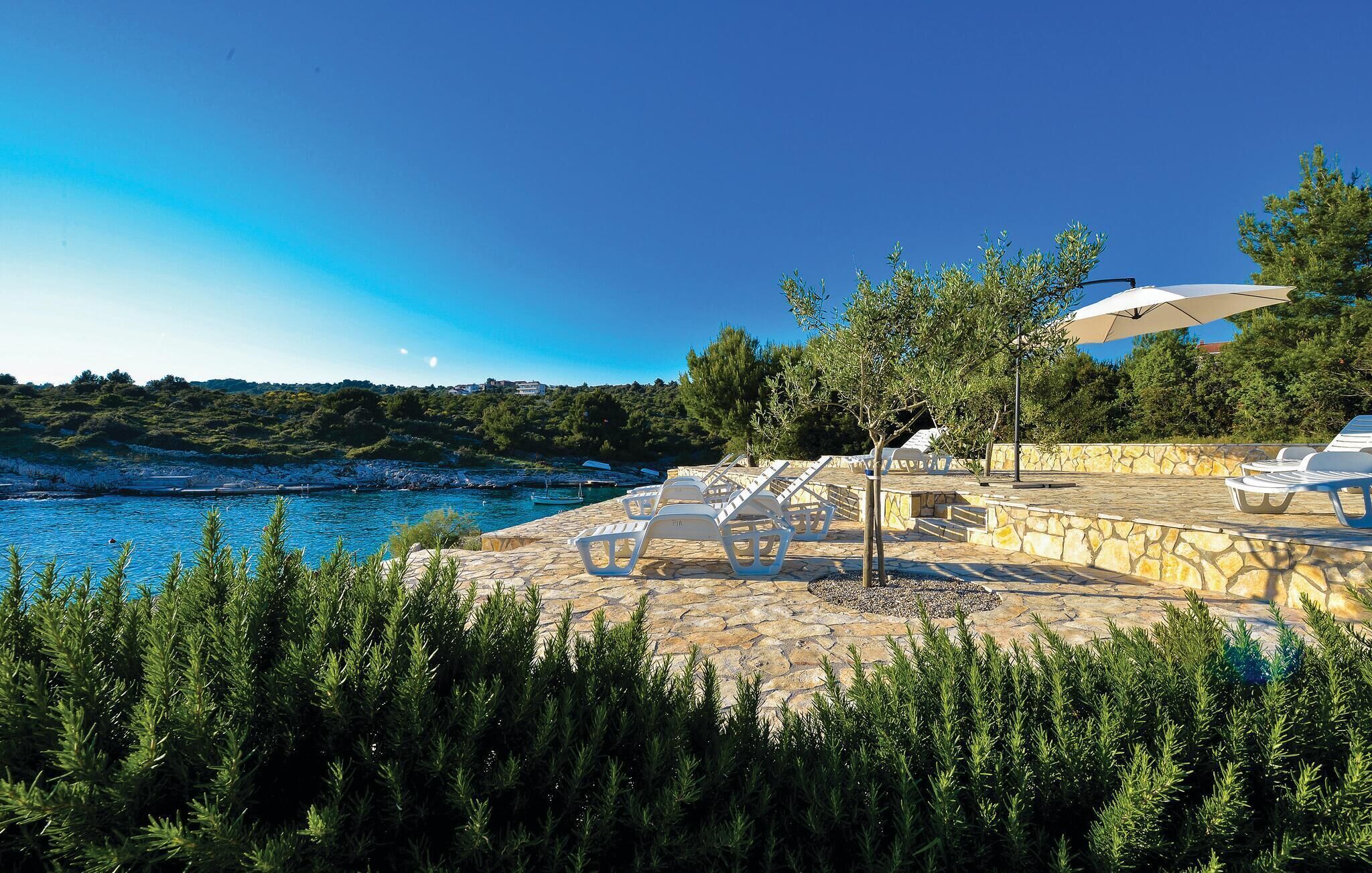 A coastal terrace with stone flooring, white lounge chairs, and a large umbrella.
