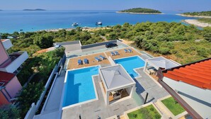 Zona de piscina en la azotea con múltiples tumbonas y una piscina pequeña, rodeada de exuberante vegetación y vistas al mar.