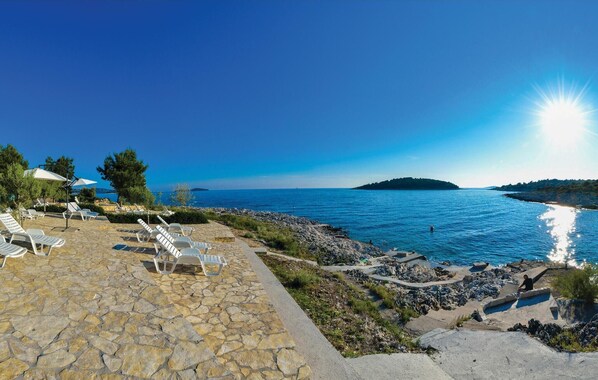 A stone patio with lounge chairs and umbrellas overlooking a rocky shoreline and the sea. - Cozy apartment in Rogoznica with sauna (Rogoznica)