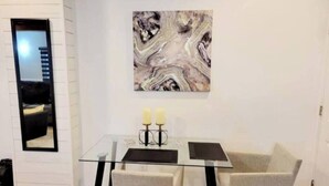 Ein moderner Essbereich mit einem Glastisch, zwei grauen Stühlen und einer Marmorbildkunst an der Wand.