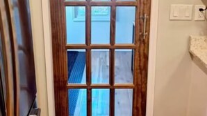 Eine Holztür mit Glasscheiben, Blick auf einen blauen Himmel und eine weiße Wand mit Lichtschalter.