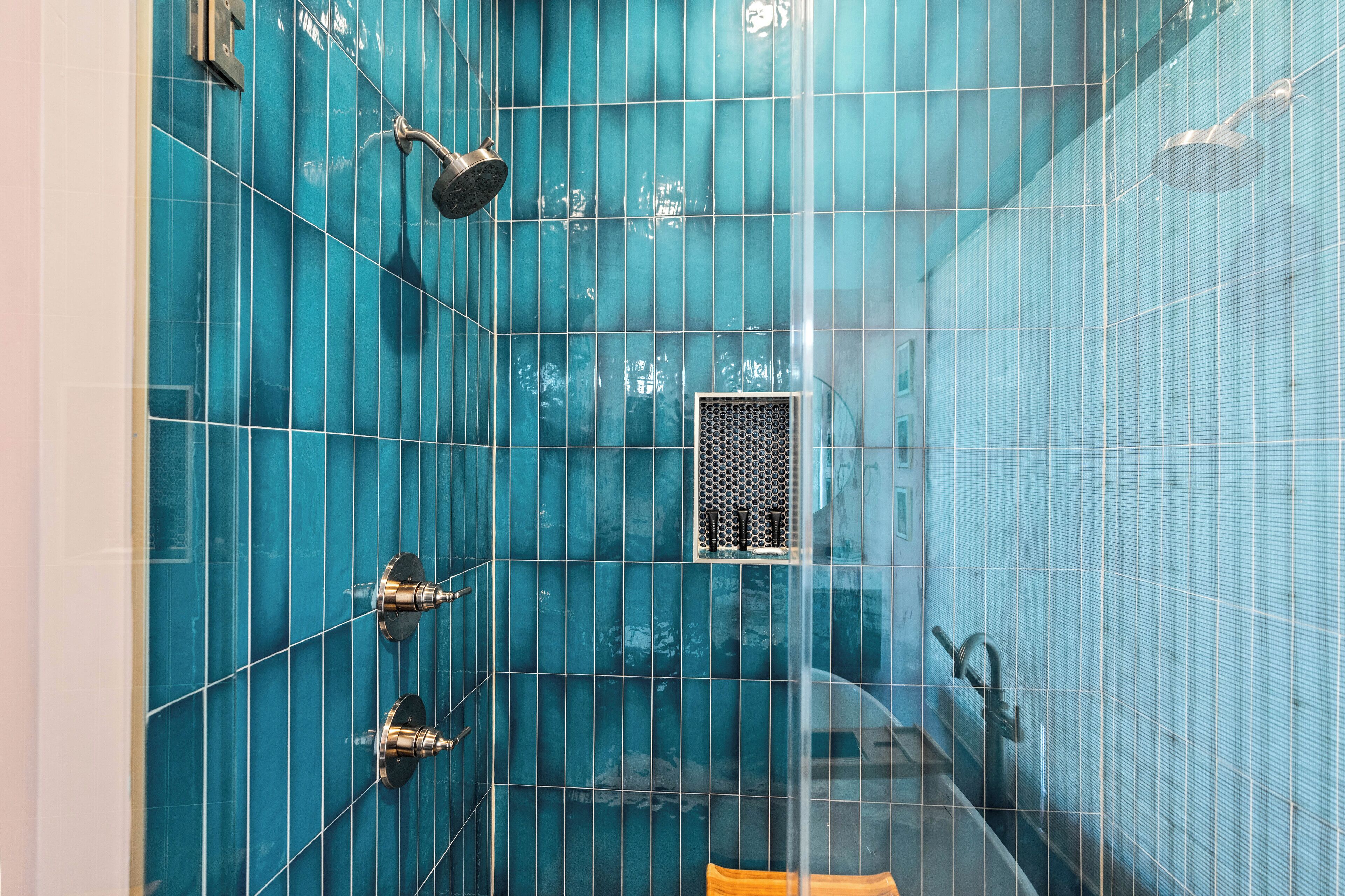 A bathroom with blue tiles, a showerhead, and a ventilation grille.