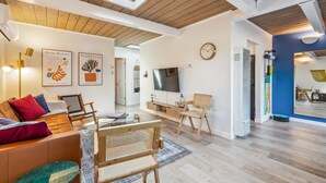 Un salon moderne avec un plafond en bois, un téléviseur à écran plat et un canapé agrémenté de coussins colorés.