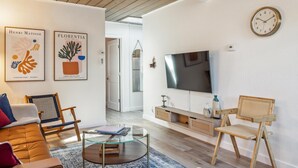 Un salon comprenant un canapé, deux fauteuils, une table basse, un téléviseur et des œuvres d’art accrochées au mur.