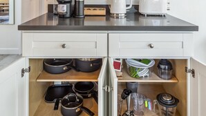 Une cuisine avec des placards ouverts où sont exposés les ustensiles de cuisine, les casseroles et une machine à café.