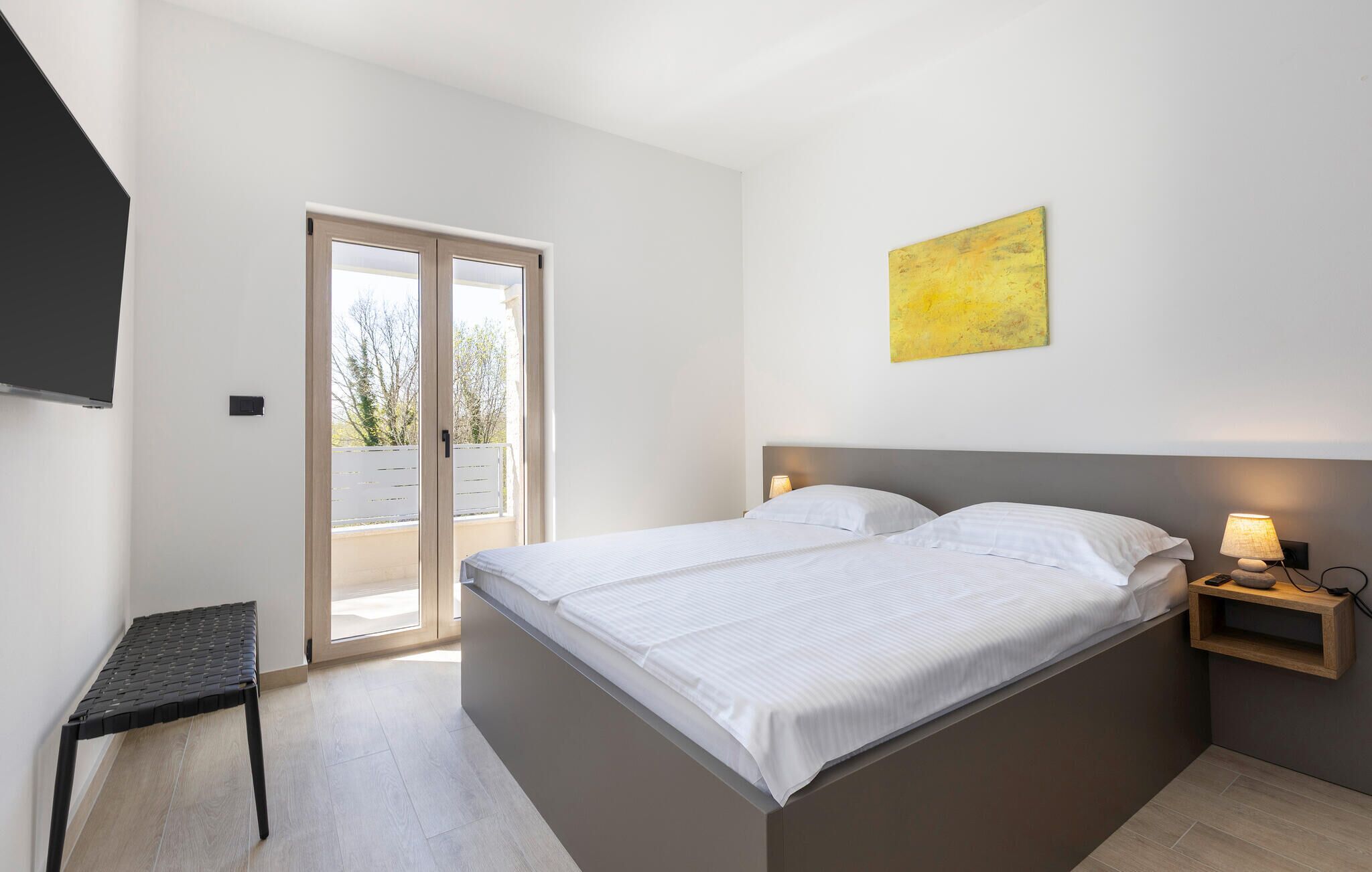 Een slaapkamer met een bed, een nachtkastje, een lamp, een schilderij en een schuifdeur naar een balkon.