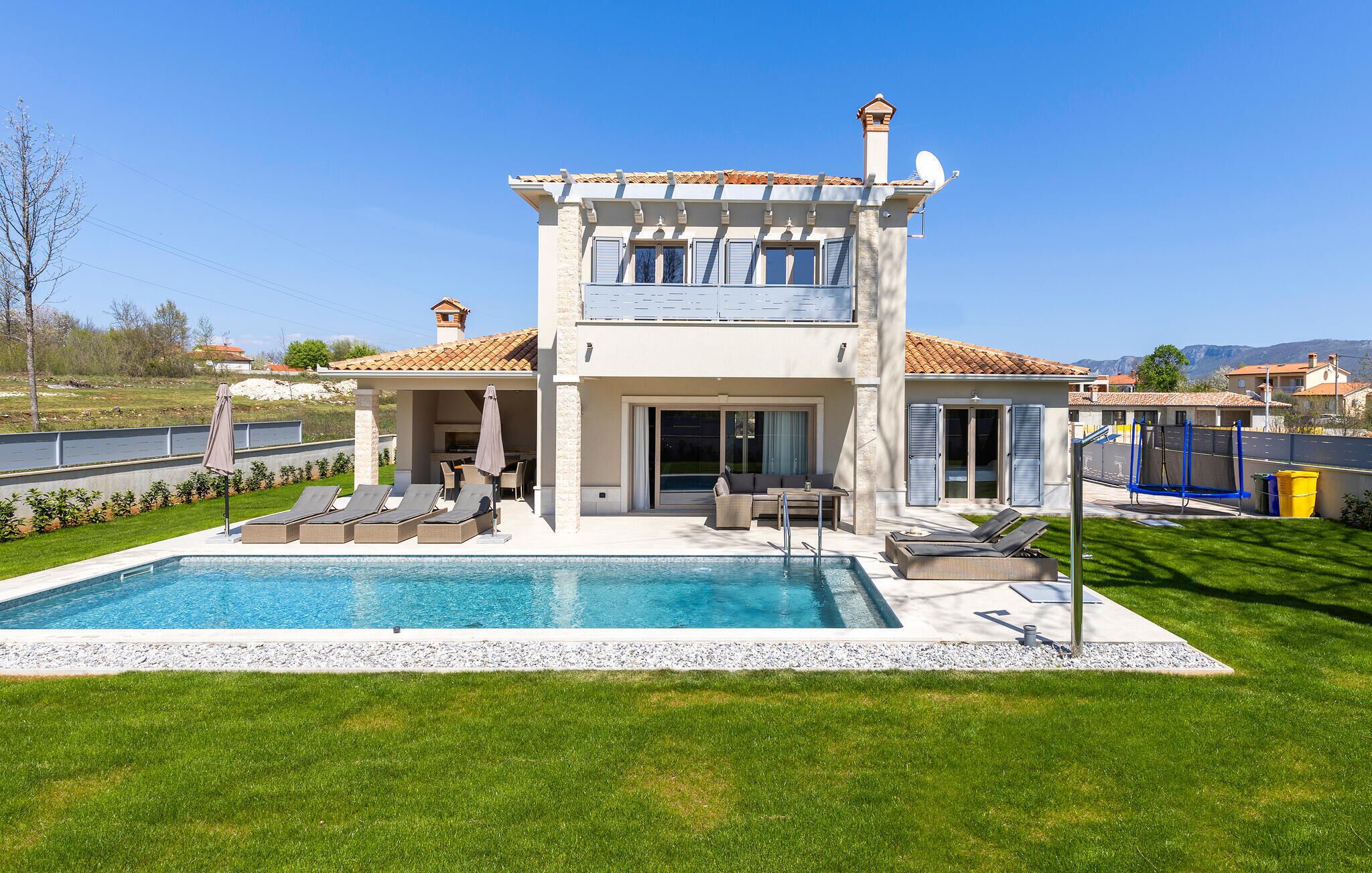 A two-story house with a swimming pool, outdoor seating, and a view of the surrounding landscape.