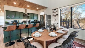 Une cuisine moderne avec des meubles de couleur verte, un réfrigérateur en acier inoxydable et un coin repas avec une table en bois, mise pour quatre personnes.