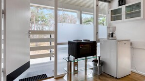 A compact kitchen with a coffee maker, a small refrigerator, and a glass-top table.