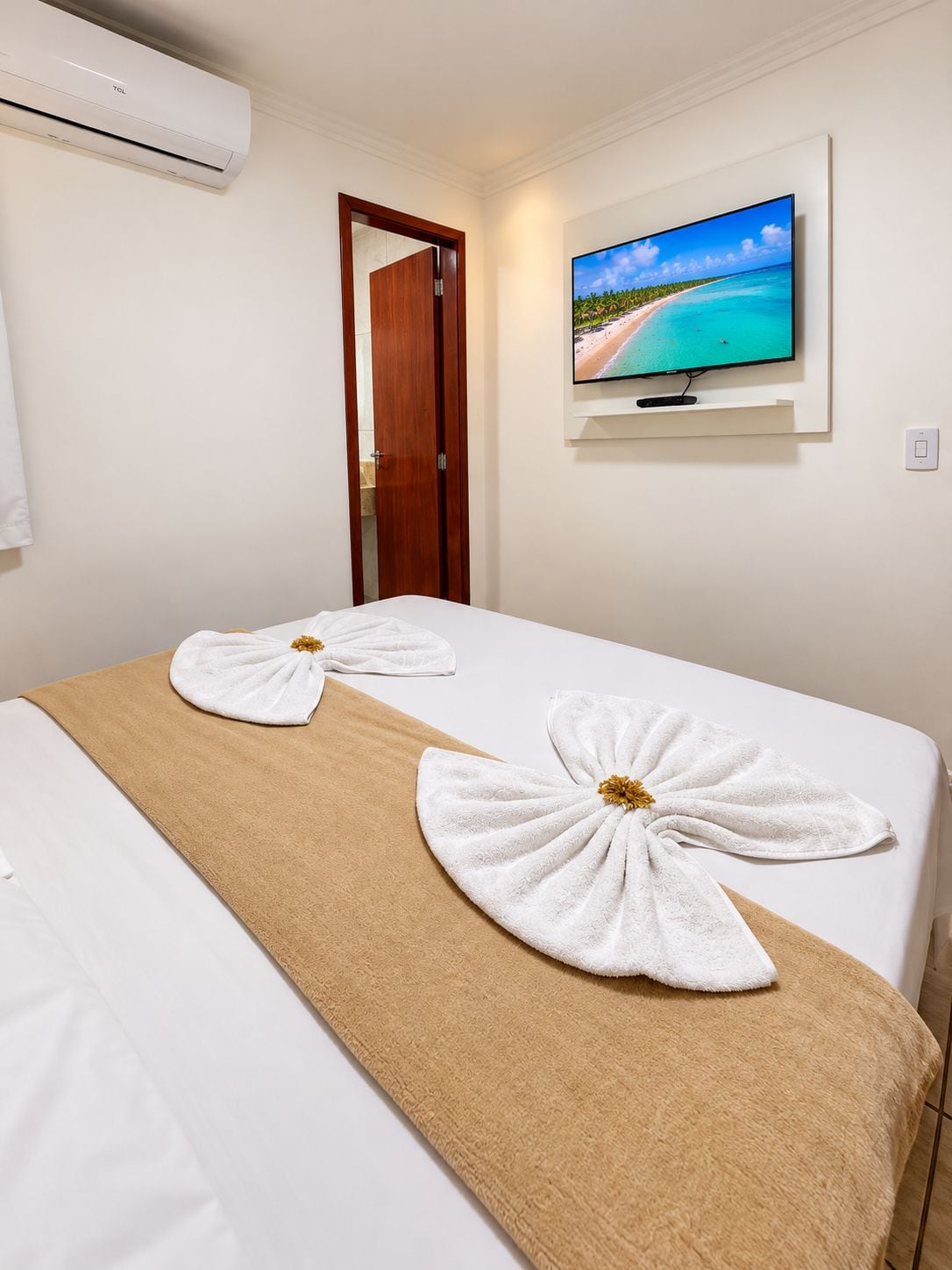 A hotel room with a bed, a TV mounted on the wall, and a door leading to another room.