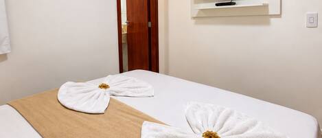 A hotel room with a bed, a TV mounted on the wall, and a door leading to another room.