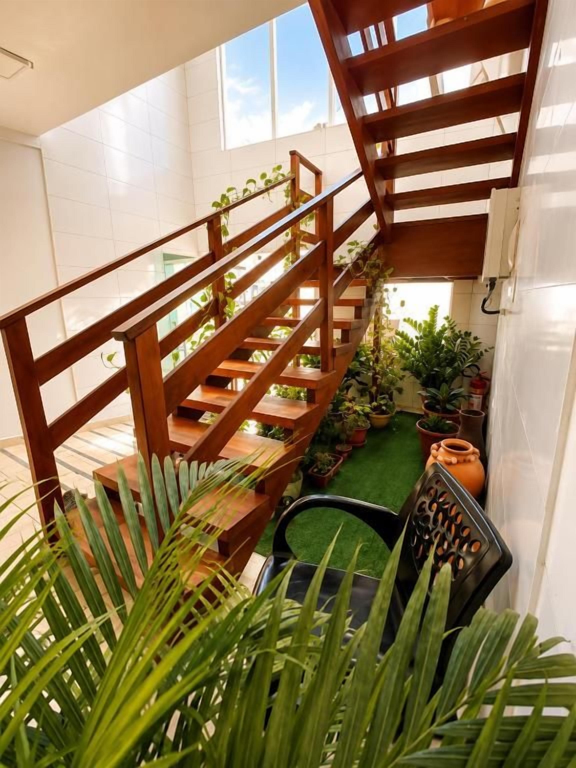 A wooden staircase with a green artificial turf landing area, surrounded by potted plants.