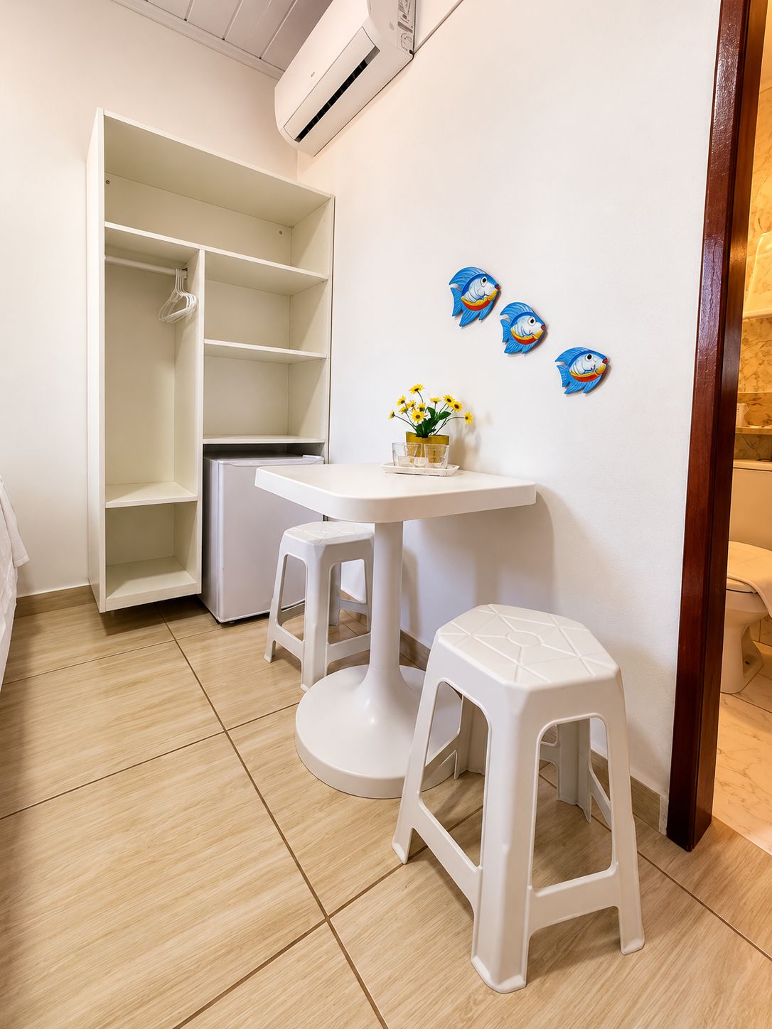 A room with a white wardrobe, a small table with a vase of flowers, and two white stools.